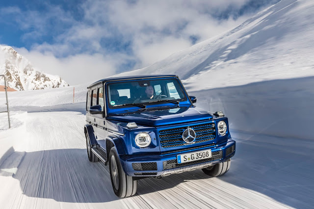 In this image, we have a new Mercedes G-Class captured in a move on a snow road with winter scenery somewhere in a mountain. The blue color of the G-Class makes a really good contrast with the white snow and it corresponds with the blue sky and some white clouds. A really nice photograph.