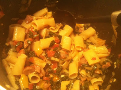 rigatoni being stirred in pot with kale and sausage sauce