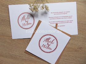 Invitación de boda doblada de estilo moderna e informal con corona de hojas y nombre de los novios en estilográfica