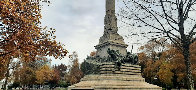 Monumento numa praça do Porto com muitas árvores outonais