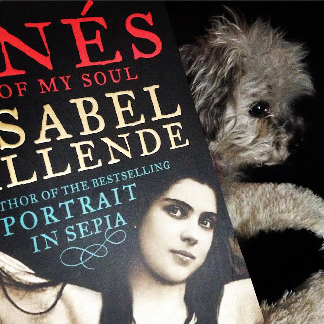 Murchie hovers behind a trade paperback copy of Inés of My Soul. The book's cover features a black and white photograph of a Latina woman with long black hair.