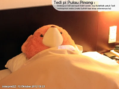 gambar seekor Teddy Bear sedang berbaring di atas katil sambil berselimut di sebuah hotel di tepi pantai di Pulau Pinang.