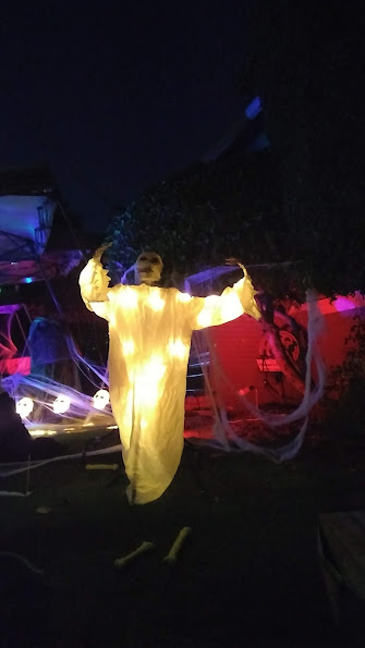 Nighttime photo of a yard with illuminated plastic skulls and a person dressed as a ghost with a mask rising up from the ground.