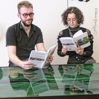 This picture features two young adults reading a book from my series, “Words In Our Beak.” They are seated at a table that has a glass-top. The man at the left is smiling as he reads volume one. He wears glasses which have a black round rim. He is wearing a black-polo shirt. Sitting at his left (but right side in the image) is a woman who is reading volume two. She is also smiling as she reads. She is wearing a dressy-looking black top and her glasses have a rim that is pale light color that it is not distinguishable. Because the table they are sitting at is glass, their faces and the books and they are reading are reflected in the table top.  Information re these books as well as info re volume three is on my blog @ https://www.thelastleafgardener.com/2018/10/one-sheet-book-series-info.html