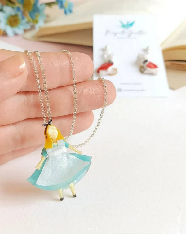 fingers holding necklace chain onto which is attached an Alice in Wonderland paper figurine