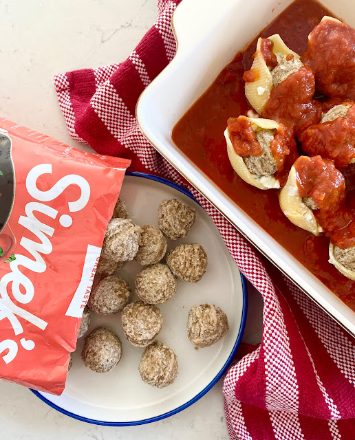 Red bag of Simek's meatballs on a white plate next to a baking dish of stuffed shells.