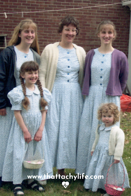 A mother and four daughters smile at the camera on Easter morning. Each of the girls is wearing a matching prairie-style dress and cardigan. The two youngest girls are holding Easter baskets. The youngest girl is Bonje at two years old. She has adorable chubby pink cheeks and strawberry blonde curls. .