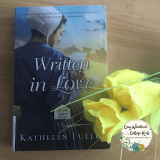 a wooden table with the book written in love next to a bunch of yellow roses