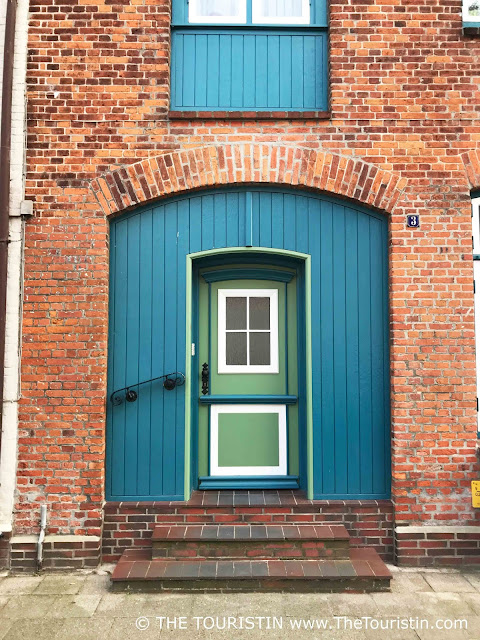 A red brick facade with a wooden door and shutters painted in light green and teal