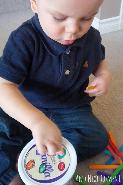 Toddler pushing popsicle sticks through a slot