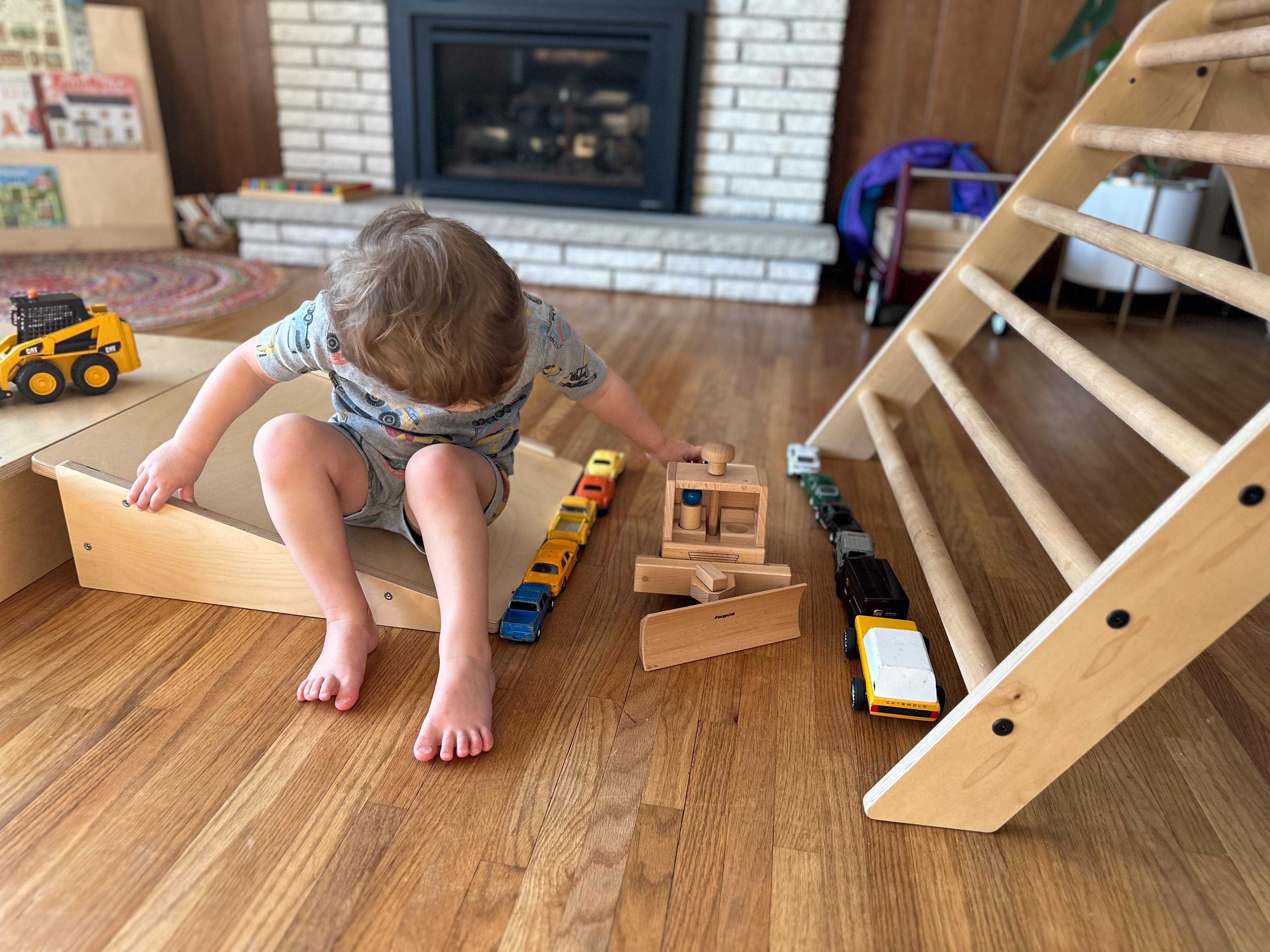 3-year-old pretends plays in his Montessori home with diecast cars and a wooden snowplow.