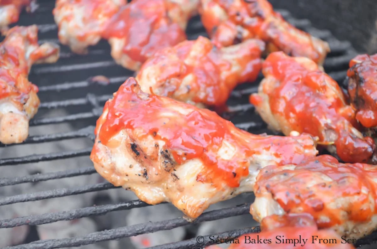 Crispy Chicken Wings being coated with Roasted Strawberry Chipotle Barbecue Sauce on a charcoal grill.