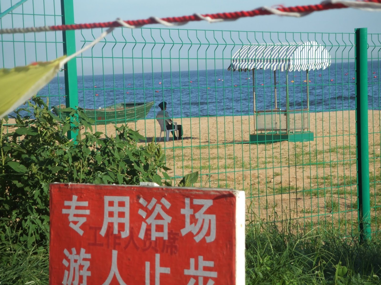 Mann in Uniform hinter grünem Zaun neben grünem Boot am Strand