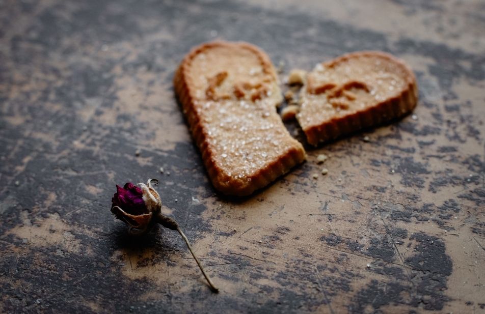 A imagem mostra um pão de forma no formato de um coração e partido com uma rosa a seu lado