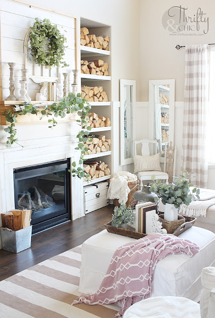 living room with white couch, large window, stacked wood, and shiplap mantel