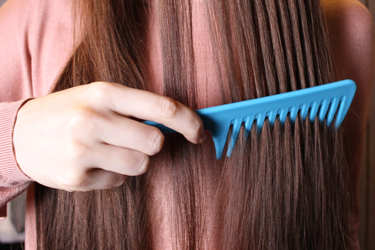 woman is combing her long hair with a wide-tooth comb