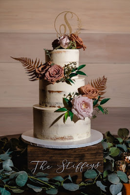 three tier naked wedding cake with floral and greenery on wooden cake stand
