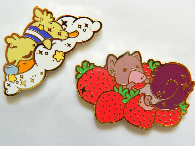 A photo showing two pin badges: one of a sleeping duck on a cloud and one of a squirrel surrounded by strawberries