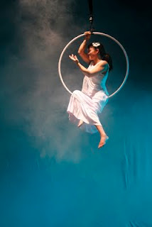 Estrela - Ceci Yeda, atriz e bailarina cadeirante, dança sorridente e suspensa numa lira, sob luz delicada e fundo azul.