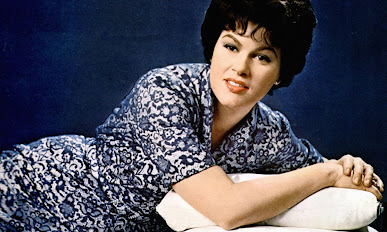 Patsy Cline color photo landscape oriented reclining in her arm wearing a blue dress