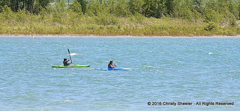 Artist's two teens kayak over the mild white caps on the lake.