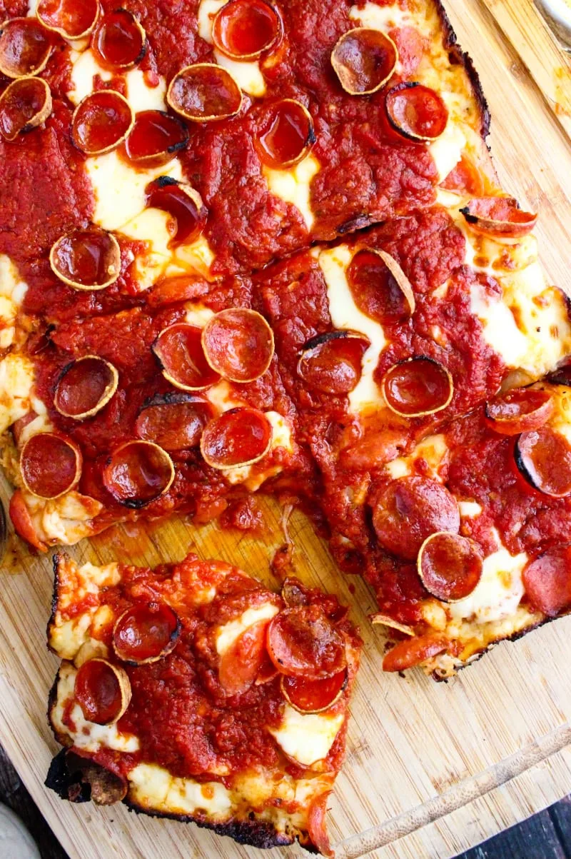 Detroit Pepperoni Pizza on a cutting board with one square slice cut and slightly separated from the rest.