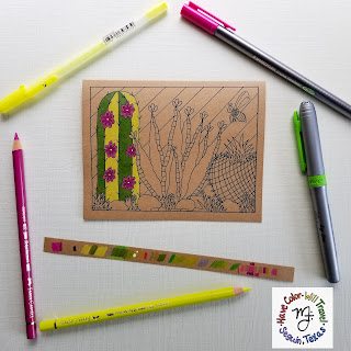 A greeting card printed on Kraft cardstock and covered with a cactus illustration to color is situated in the center of the photo on a white background and surrounded by art supplies.