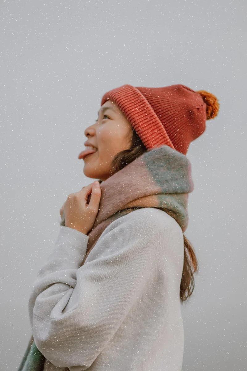 woman in brightly-colored beanie cathes snow with her mouth