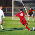 Football iu 1996.jpg. An attacking player (No. 10) attempts to kick the ball past the opposing team's goalkeeper and between the goalposts to score a goal