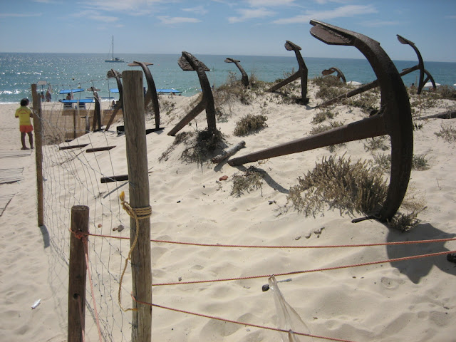 kotwice ustawiona na wydmnie poprzedzającej plażę do Barril w Algarve, w tle błękitne, spokojne morze z żaglówką 