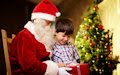 Santa Claus dándole un regalo a un niño junto al Arbol de Navidad