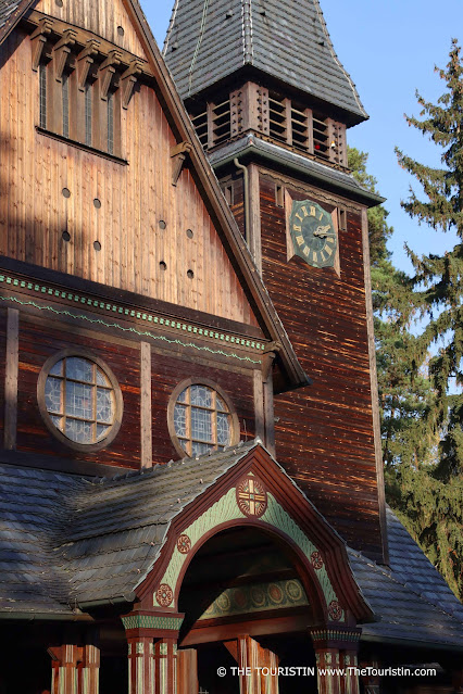 Ornamented facade of a dark brown wooden stave church under a bright blue sky.