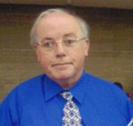 William Elliott, poses for the camera, wearing a deep blue shirt and silver grey tie.