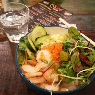 A large blue and white circular bowl filled with white rice, pieces of light brown chicken and a selection of colourful vegetables in a light clear sauce on a large light brown rectangular table on a white background 