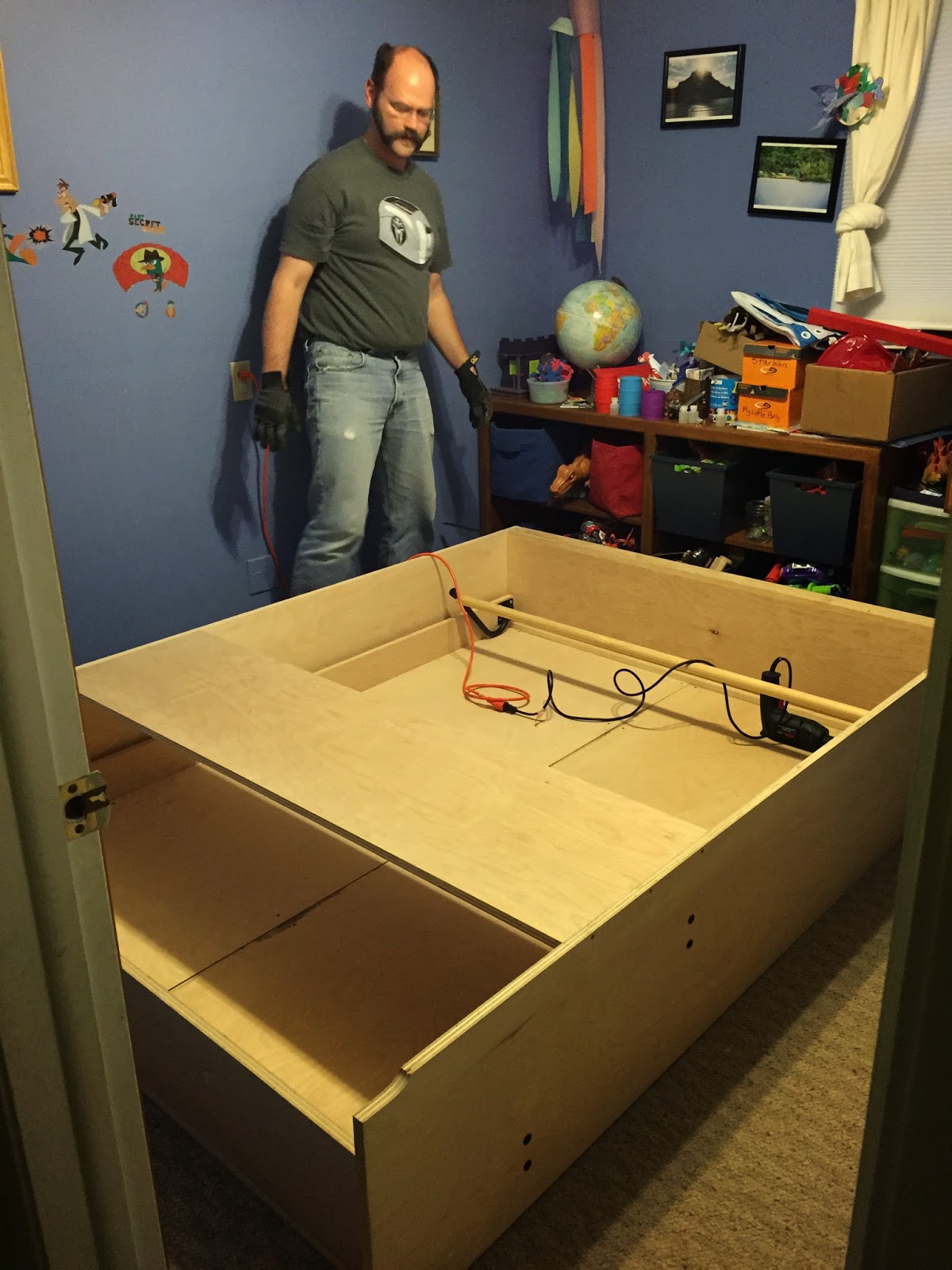 Chris standing next to the Murphy bed and frame while assembling it in the playroom guest room.
