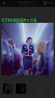 По салону самолета проходит девушка стюардесса в синем костюме