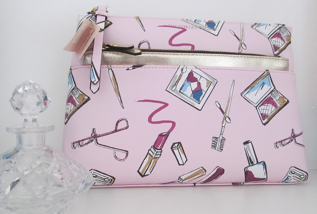 pale pink makeup bag with illustrations of eyelash curlers, lipsticks and eyeshadow palettes and crystal decanter on left