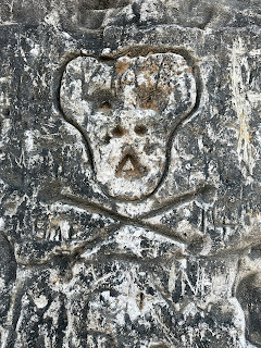 A photo showing a primitive looking skull and crossbones carved into the white chalk cliffs at Botany Bay.  The chalk around it is dirty and dark.  Photo by Kevin Nosferatu for the Skulferatu Project.