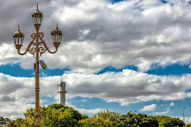 Un conjunto de tres faroles bajo una imponente nube blanca en el cielo.