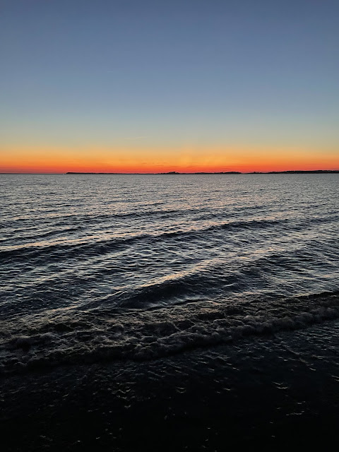 A view of the ocean at high tide with the sun having just set. The sky is a twilight color with the horizon being a pinkish orange.