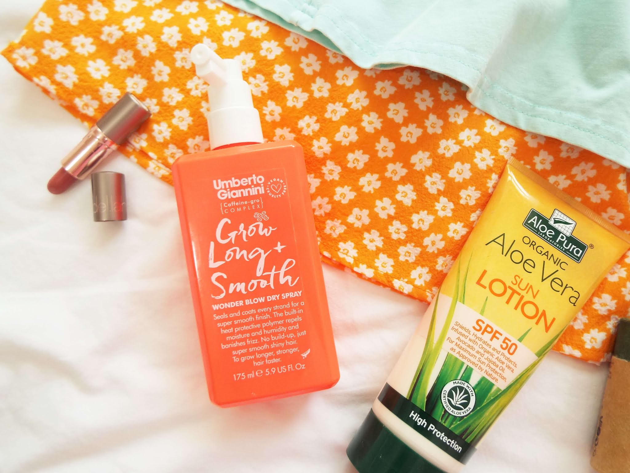 Close-up flatlay picture of monthly favourite heat protectant, SPF and lipstick, lay on orange floral dress.