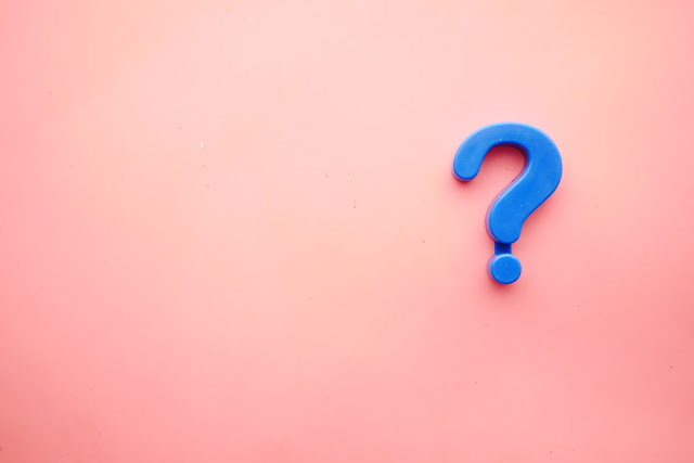 A blue piece of plastic in the shape of a question mark rests against a red background.