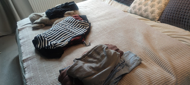 An image of a bed with three piles of clothes being sorted to donate, bin or sell.