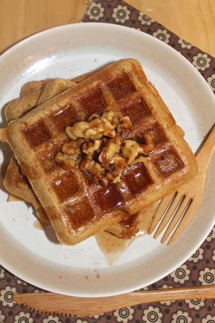 Plate of whole wheat acorn squash waffles topped with walnuts and cinnamon maple syrup.