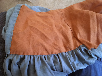 A rusty-orange yoke lining, pinned into a muted-teal skirt, with the skirt fabric folded over the yoke at left to make a wide button band, and the gathered-on skirt showing just below the yoke lining.