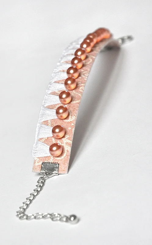 peach and white stitched paper bracelet with peach pearl accents and silver chain fastener