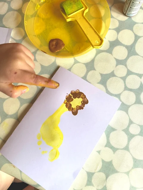 Toddler fingers putting a finger print mane on a yellow footprint lion