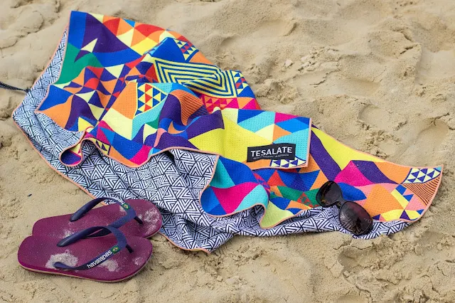 A colourful towel, flip flops and sunglasses on sand