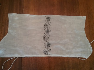 Rectangular piece of flat linen that has been cut and hemmed with curves along the two short sides. Three repeated motifs make an embroidered  stripe down the center. Each motif is an S-shaped vine connecting an oak leave to a cluster of three acorns. The leaves and acorns are sparsely filled in with spaced stitches in lattices, lines, and alternating X and O shapes.