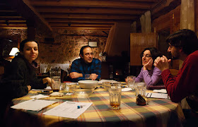 Four gamers sitting at a table playing Dungeons and Dragons. There are character sheets, dice, and pencils on the table, as well as empty food bowls and several empty (or almost empty) drink glasses, indicating that the game is at an end.